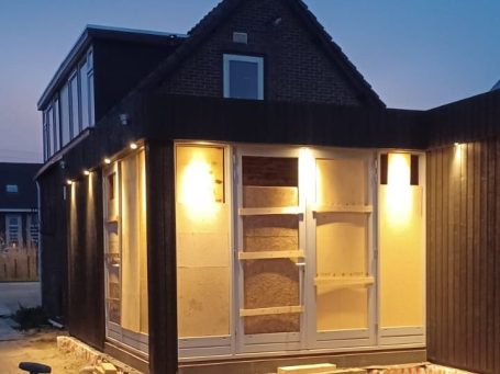 Moderne zwart houten woning met verlichte veranda in de schemering.