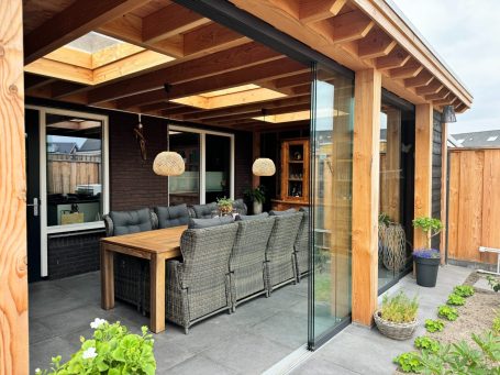 Veranda met glazen schuifdeuren, houten plafond, en een gezellige zithoek.