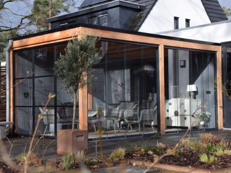 Moderne overkapping met glazen wanden, houten raamwerk en tuinmeubilair.
